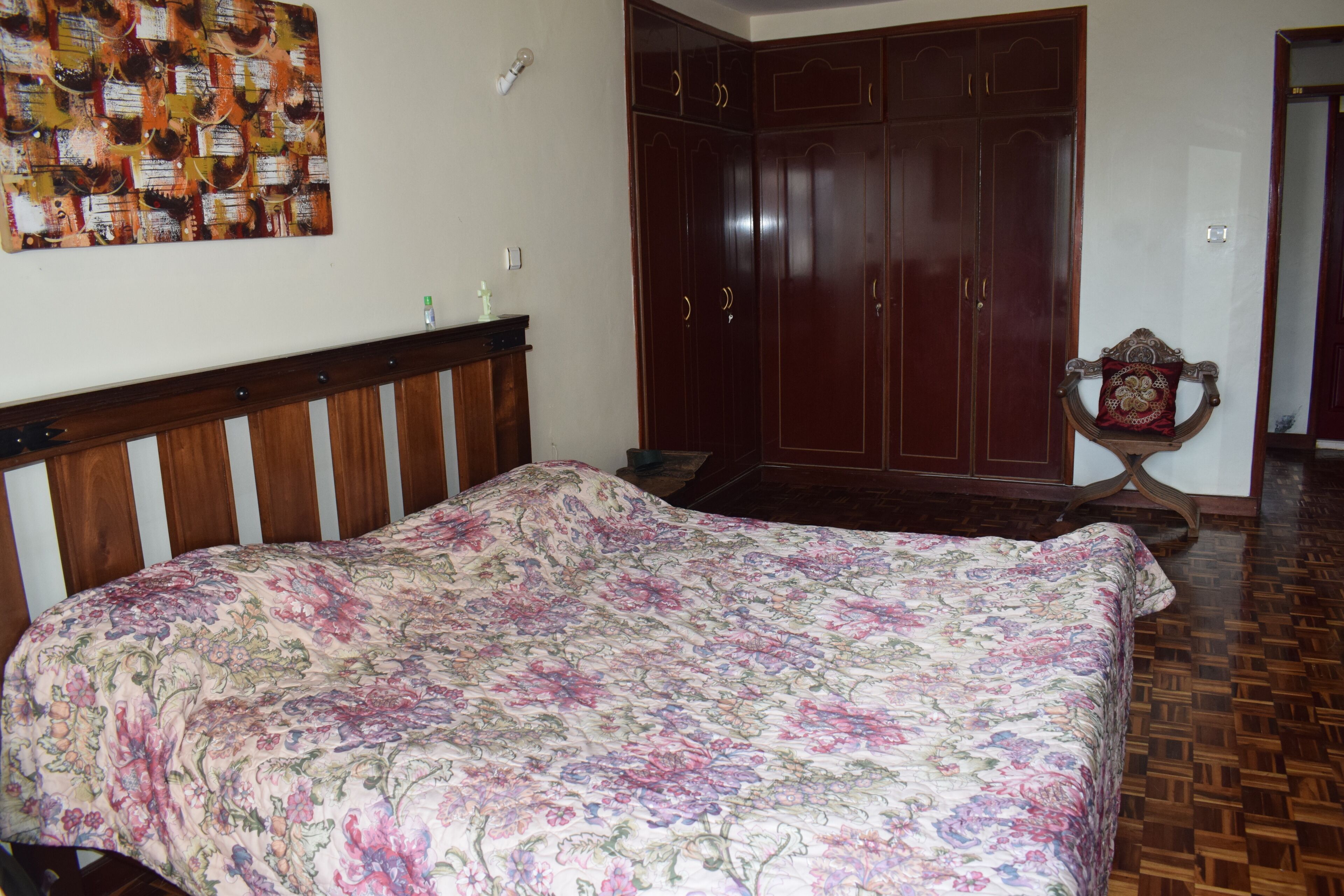 A bedroom with a floral bedspread, wooden wardrobe, and a mirror with a decorative frame.