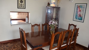 Un comedor con una mesa y sillas de madera, un florero con flores, un aparador y un cuadro en la pared.