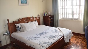 Un dormitorio con una cama de madera, una mesita de noche, un aparador y una ventana con barrotes.