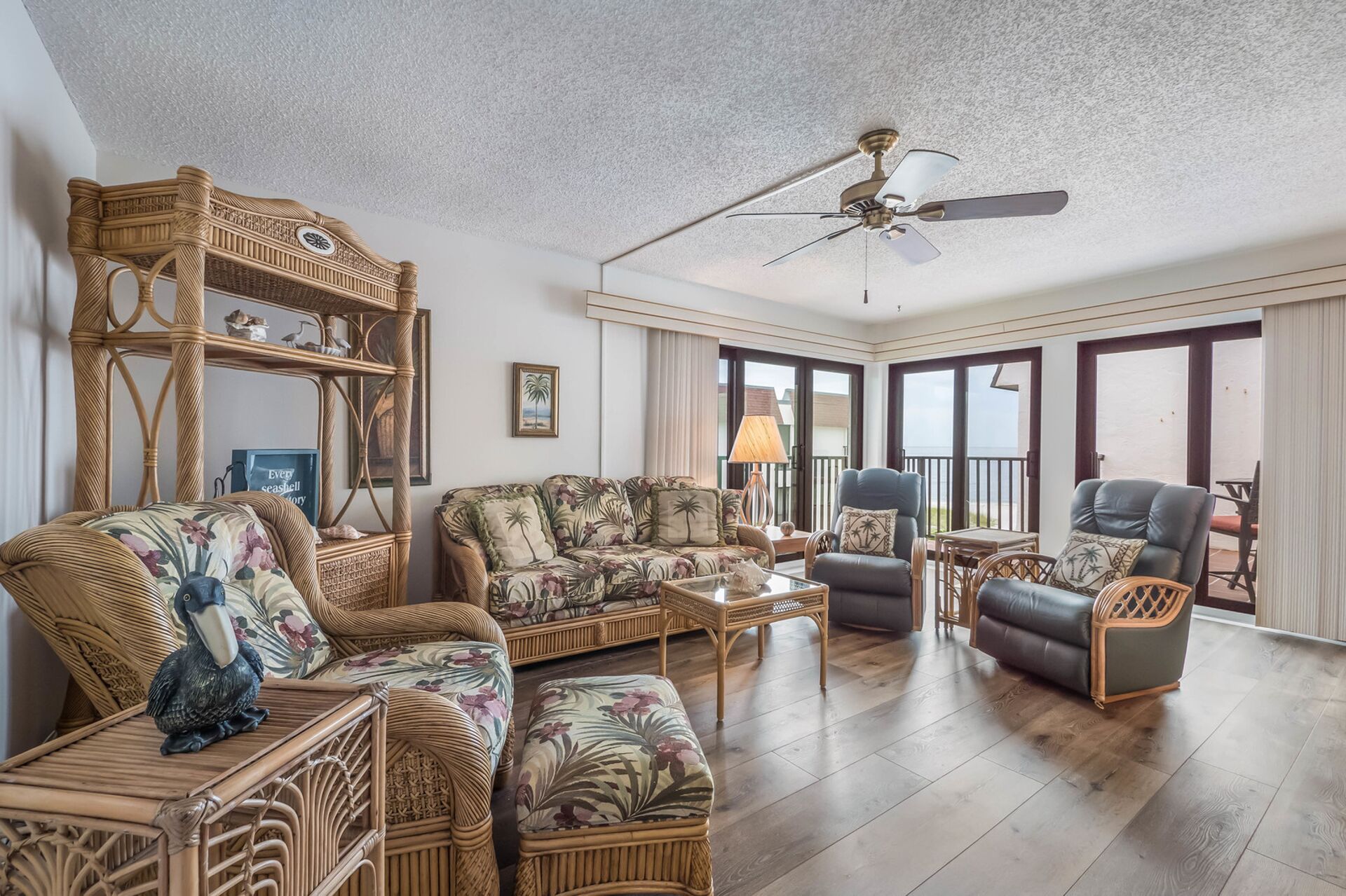 A spacious living room with a high ceiling, wicker furniture, and a view through large sliding doors to the outside.