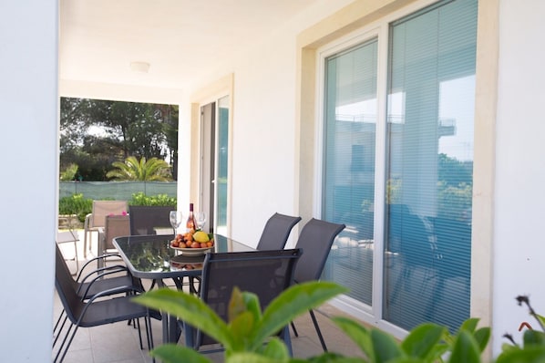 A balcony with a table set for two, featuring a fruit bowl and two wine glasses.