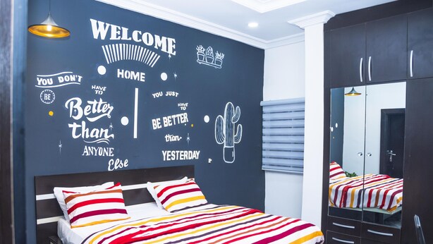 A modern bedroom with a bed, a mirror, and motivational wall art. - Lineech Apartments (Abuja)