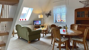 A cozy loft-style room with a sloped ceiling, a television, a dining table with chairs, and a wooden cabinet.