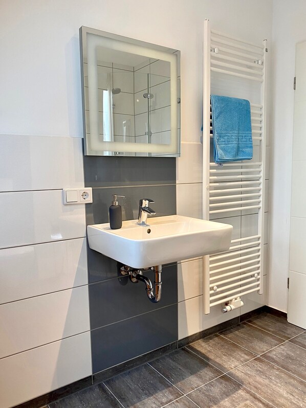 A bathroom with a white sink, a mirror, a towel rack with a blue towel, and a radiator.