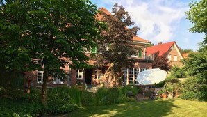 A brick house with a red roof, surrounded by lush greenery and a well-maintained lawn.