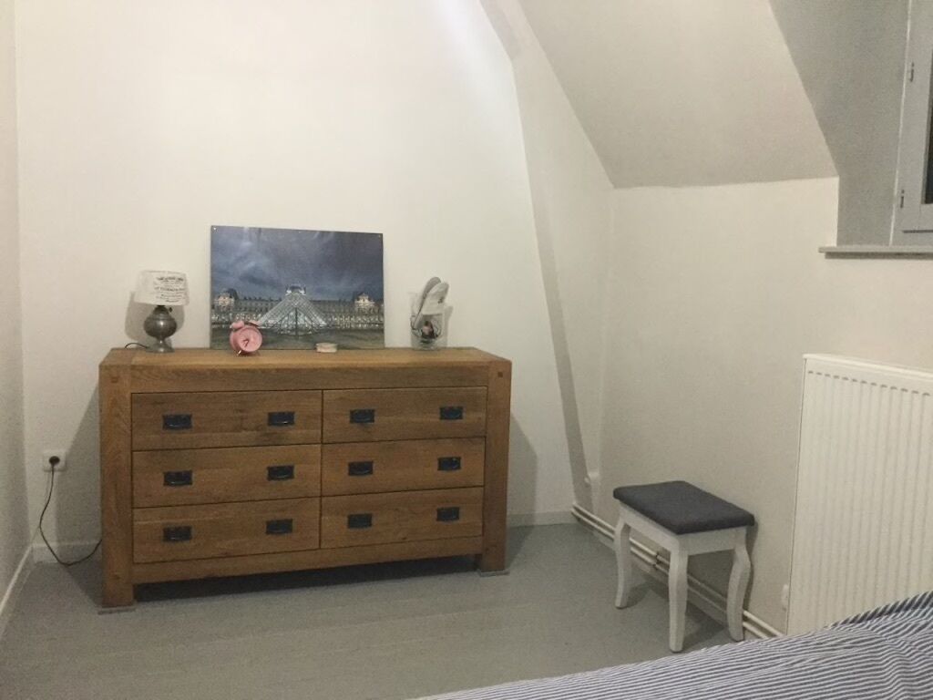 Quarto com penteadeira de madeira, um banquinho, uma pintura e um radiador.