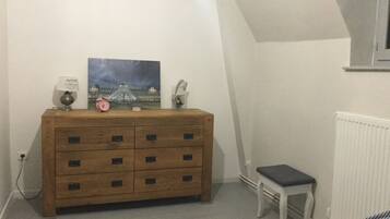 Quarto com penteadeira de madeira, um banquinho, uma pintura e um radiador.