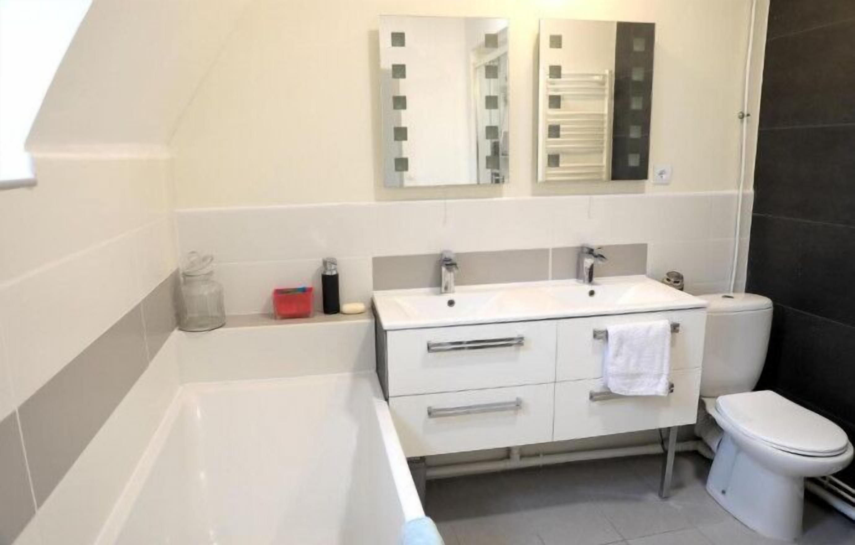 Une salle de bain moderne équipée d’une baignoire, d’un lavabo, de toilettes et de deux miroirs.