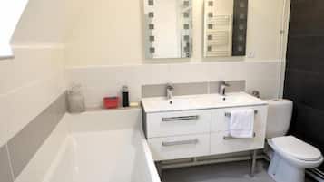 Une salle de bain moderne équipée d’une baignoire, d’un lavabo, de toilettes et de deux miroirs.
