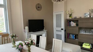 A living room with a fireplace, a television, a bookshelf, and a dining area with a table set for two.