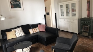 Uma sala de estar com um sofá preto, duas poltronas, uma mesa redonda pequena, um aparador com portas de vidro e um fogão antigo.
