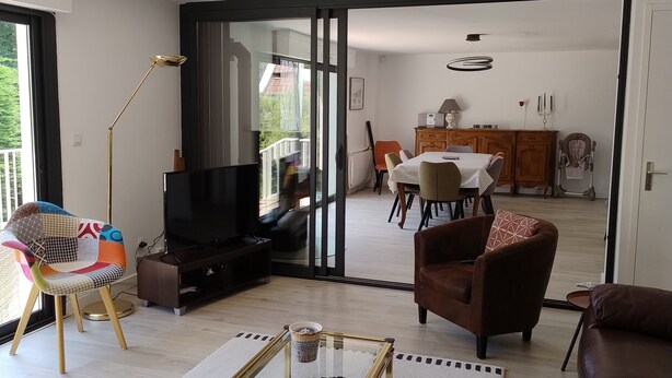 Ein modernes Wohnzimmer mit einem Glastisch, einer Couch, einem Fernseher und einem Essbereich im Hintergrund.