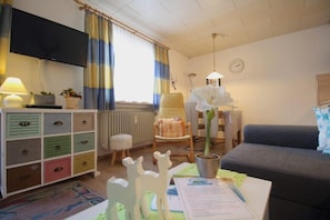 Ett mysigt vardagsrum med en soffa, ett litet bord, en lampa, en tv och ett skåp med lådor.