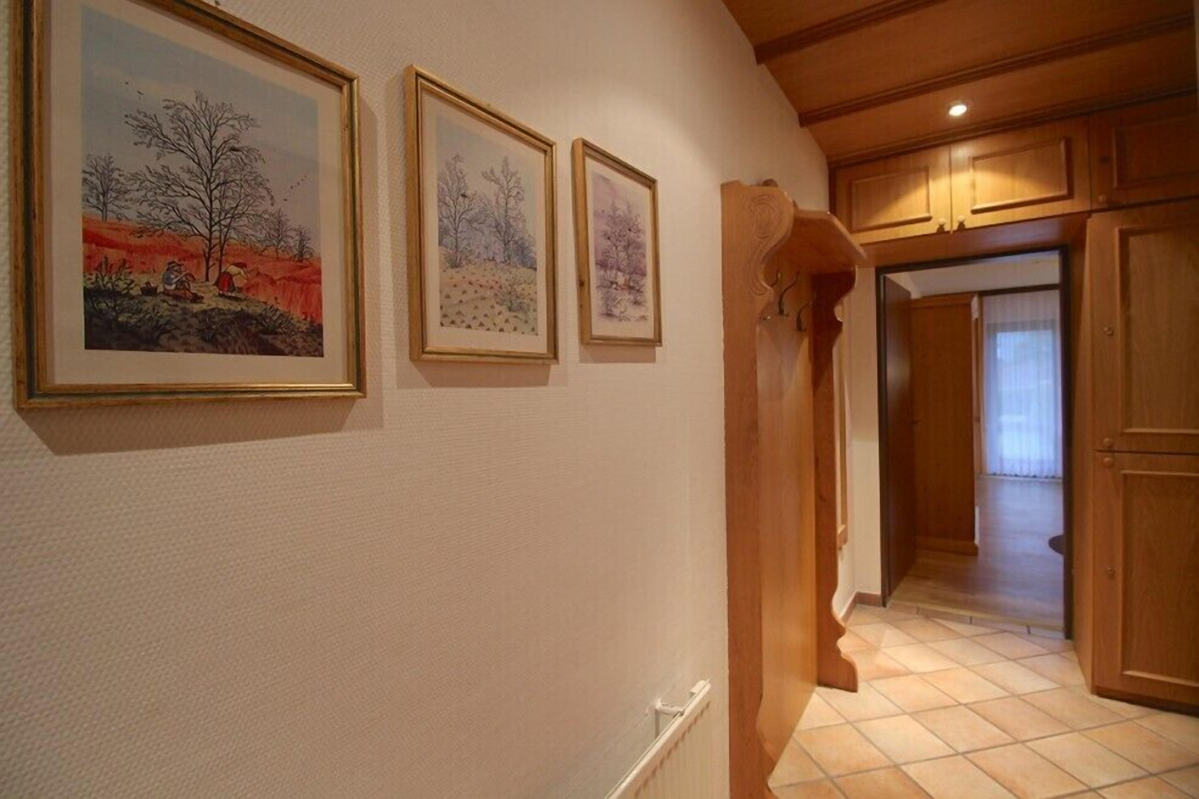 A hallway with three framed paintings on the wall, wooden cabinets, and a tiled floor.