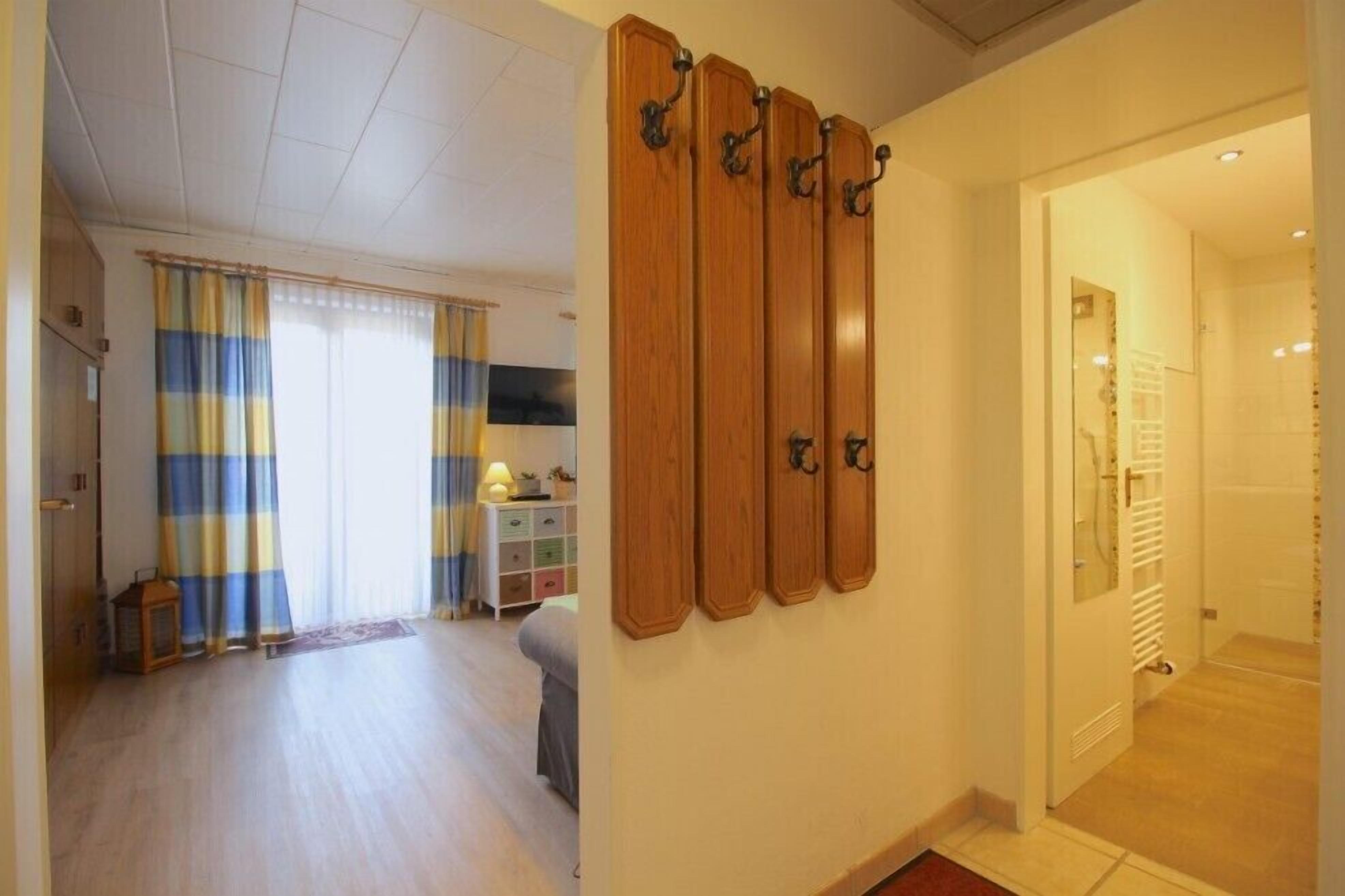 Een hotelkamer met een houten kapstok, een bed, een nachtkastje en een raam met gordijnen.