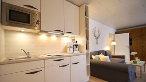 A compact kitchen with a microwave, sink, and coffee maker. There is a sofa and a small table with a vase in the living area. - Farchanter Alm (Farchant)