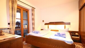 A bedroom with a wooden bed, a bedside table, a nightstand, a lamp, and a window with curtains. - Farchanter Alm (Farchant)