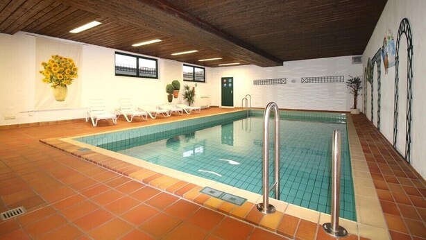 An indoor swimming pool with tiled flooring, lounge chairs, and potted plants. - Farchanter Alm (Farchant)