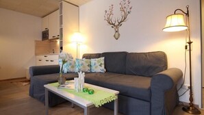 A living room with a grey sofa, a small table with a green tablecloth, and a wall-mounted deer head decoration. - Farchanter Alm (Farchant)
