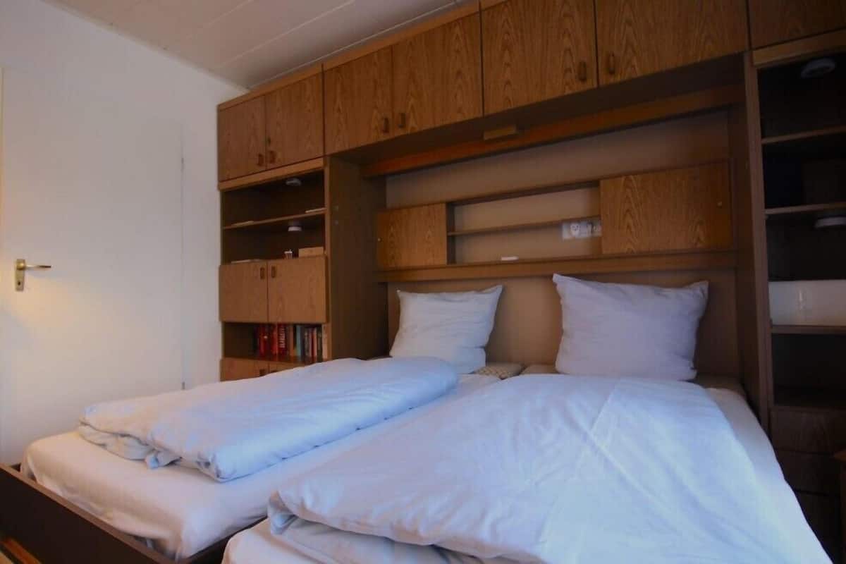 A bedroom with two beds, wooden cabinets, and a shelf unit.