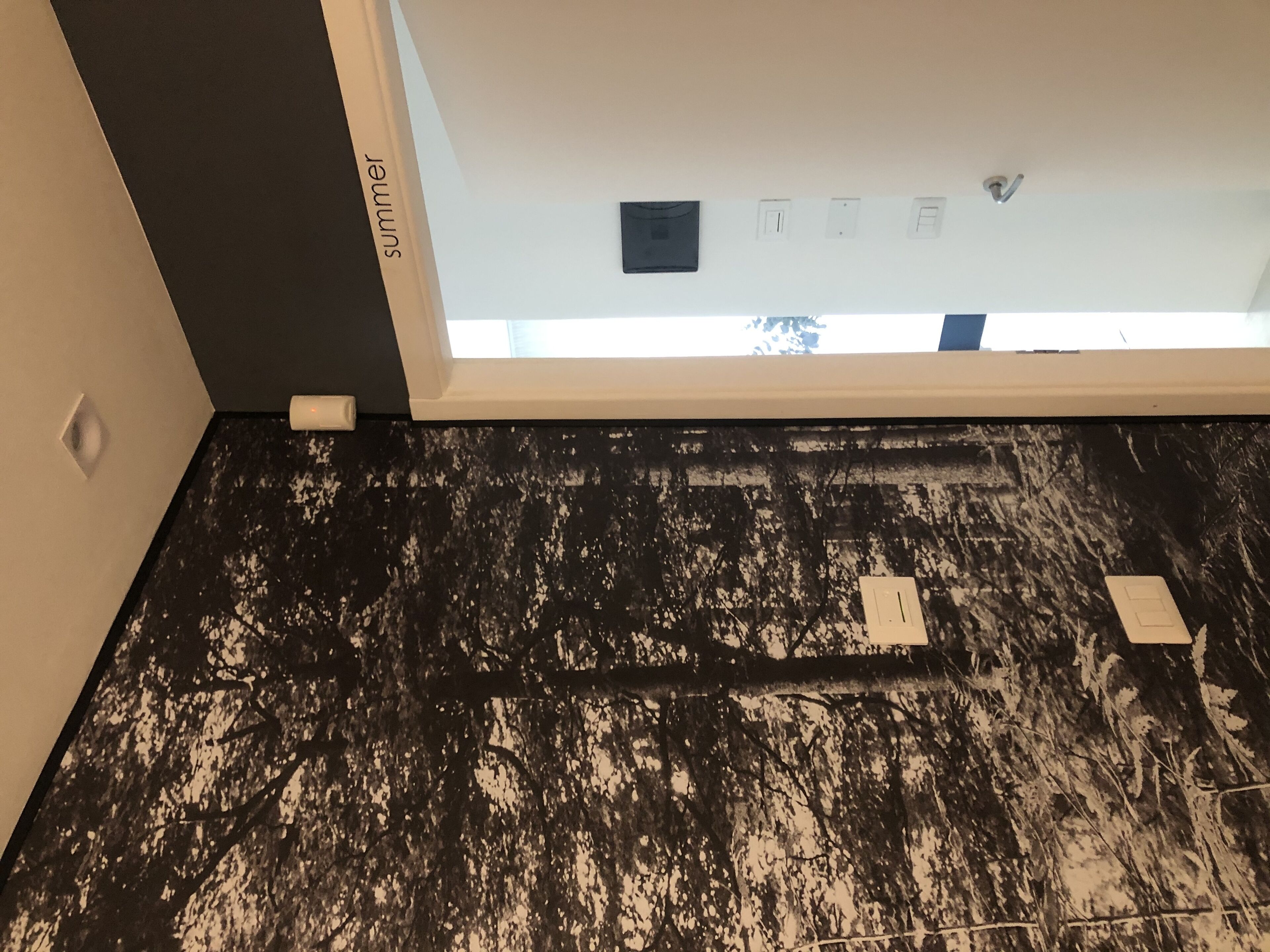 Une pièce avec un sol à motifs noir et blanc, un plafond blanc agrémenté d’une lucarne et un mur sur lequel est affiché un panneau indiquant « été ».