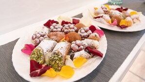 Ein Teller mit verschiedenen Pasteten und Desserts, darunter Cannoli und andere Süßspeisen, dekoriert mit Blütenblättern.