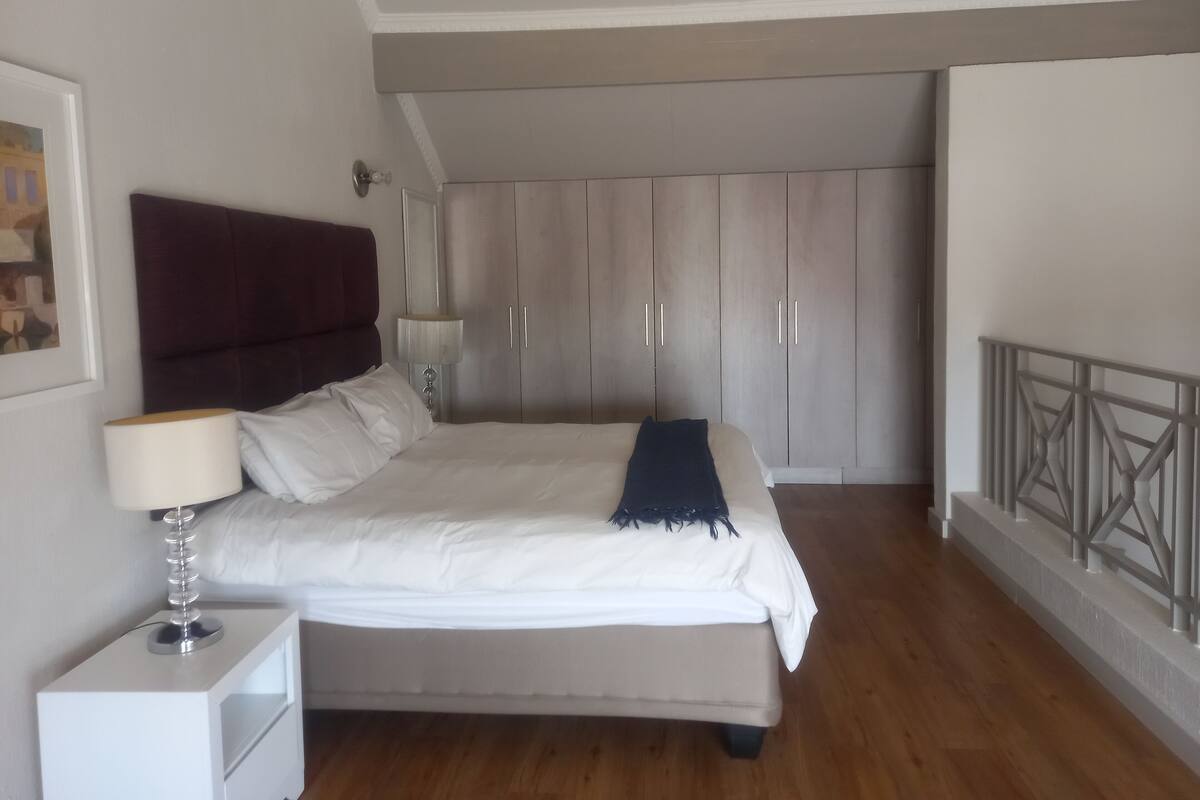 A bedroom with a bed, bedside table, lamp, wardrobe, and a painting on the wall.