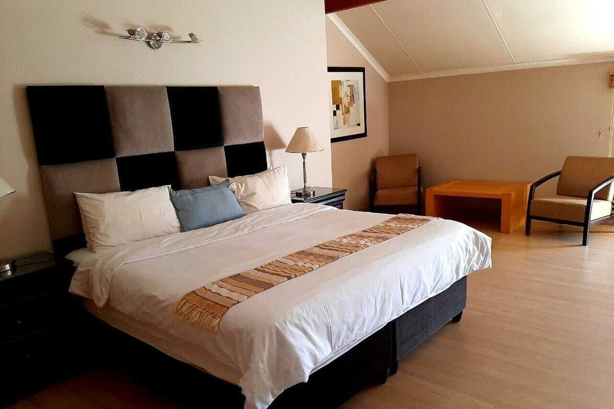 A hotel room with a large bed, a nightstand, a desk, a chair, and a lamp.