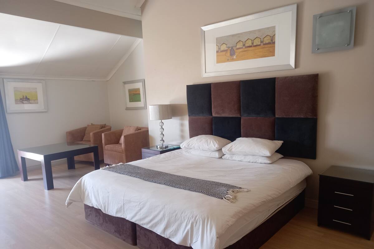 A modern hotel room with a large bed, a desk, a chair, and a lamp.