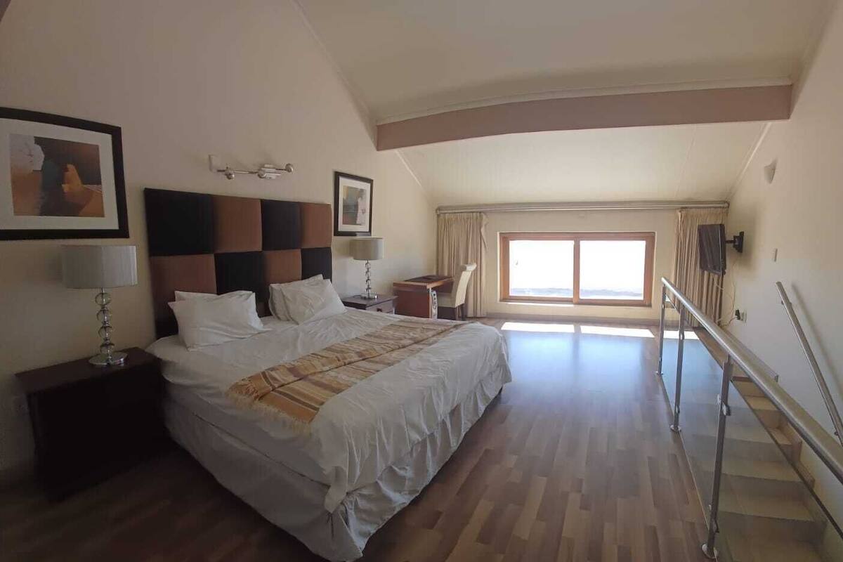 A hotel room with a large bed, a nightstand, a lamp, a picture on the wall, and a window with curtains.