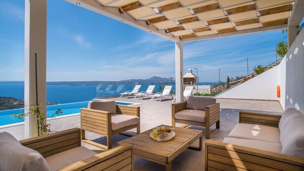 Un espace extérieur aménagé, abrité et doté de mobilier en bois, avec une piscine et une vue sur la mer.