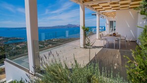 Une terrasse extérieure moderne offrant une vue dégagée sur la mer et les montagnes lointaines.