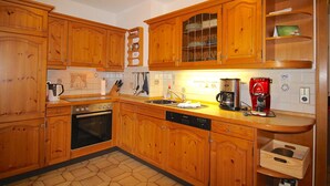 A kitchen with wooden cabinets, a stove, a dishwasher, and a coffee maker. - Chalet Adriana (Garmisch-Partenkirchen)