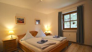A double bed with white linens, two bedside tables with lamps, a window with curtains, and two framed pictures on the wall. - Chalet Adriana (Garmisch-Partenkirchen)