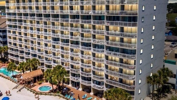 A multi-story hotel with balconies, a pool area, and lounge chairs. - 1011 Waters Edge Resort 2 Bedroom Condo by RedAwning (Murrells Inlet)