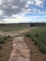 Un sendero de piedra que lleva a una construcción rústica, con un campo cercado al fondo.