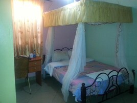 Un dormitorio con una cama bajo un dosel, un escritorio con una silla y cortinas en la ventana.