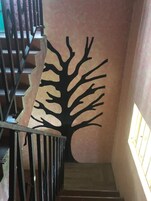 Una escalera con un diseño similar a un árbol en la pared, barandas de metal y una ventana a la derecha.