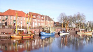 Ein Hafen mit mehreren vertäuten Booten, ein Backsteinhaus mit roten Dächern und eine ruhige Wasseroberfläche, die Boote und Gebäude spiegelt.