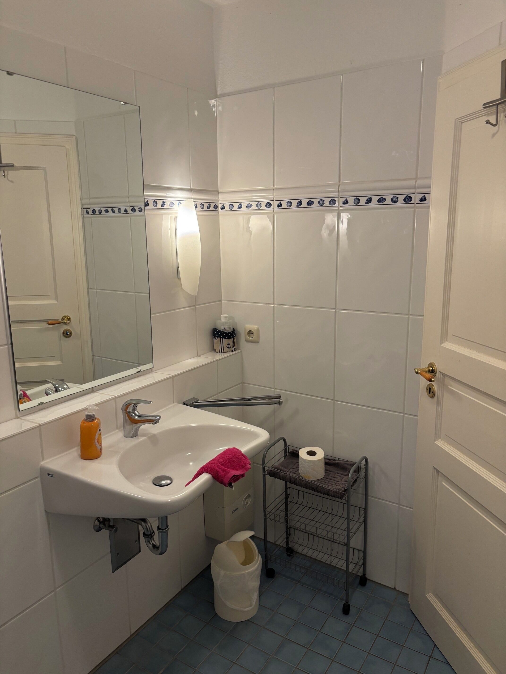 A bathroom with a sink, mirror, towel rack, and a small storage shelf.