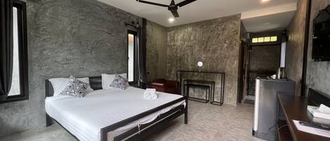 Una habitación de hotel moderna con una cama grande, un ventilador de techo, un televisor de pantalla plana y un pequeño rincón de estar con una mesa y sillas.