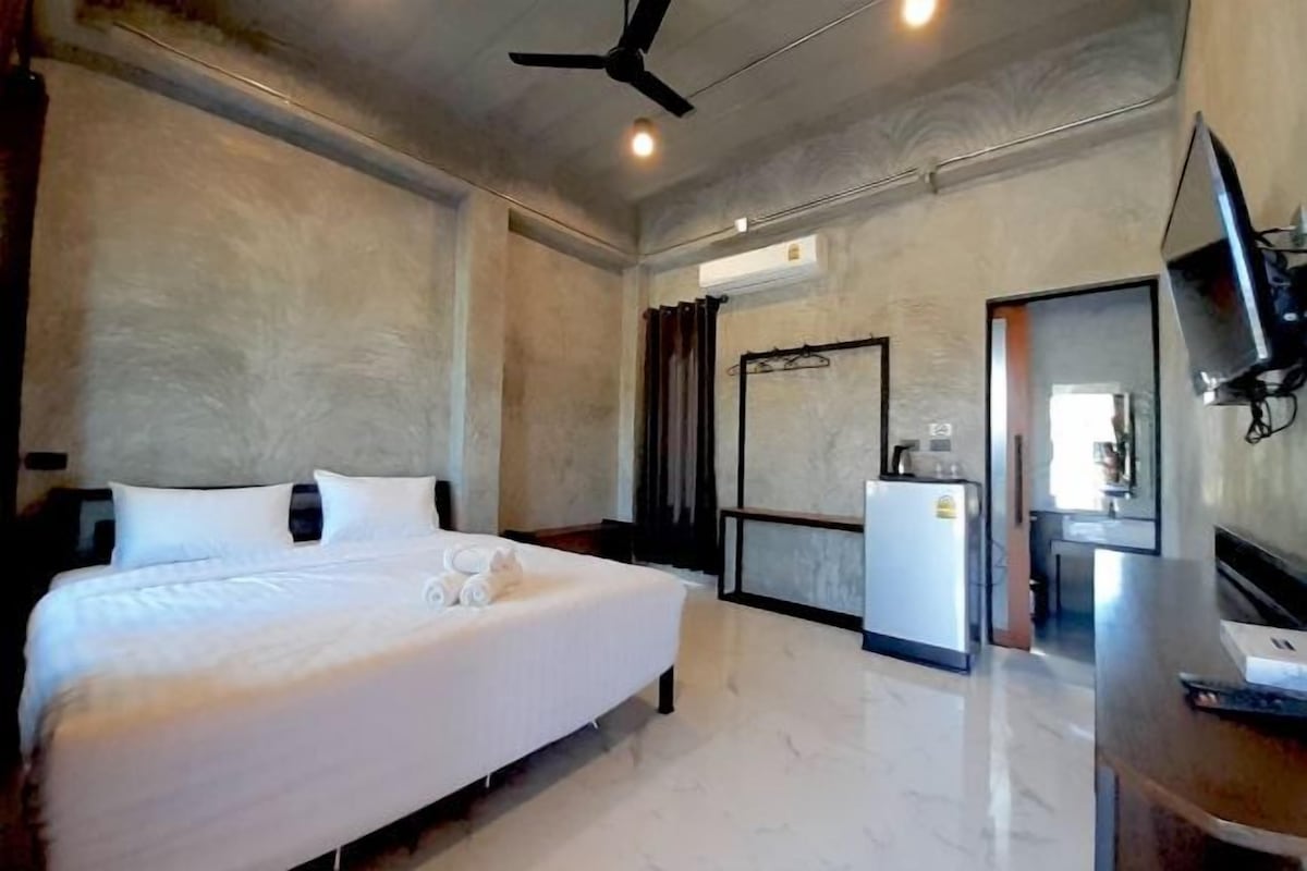 A hotel room with a bed, a television, a ceiling fan, and a small kitchenette.