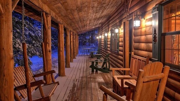 A log cabin with a wooden porch, outdoor seating, and a view of snow-covered trees. - Charming Adirondack Log Cabin PRIVATE BEACH ACCESS to Mirror Lake (Lake Placid)