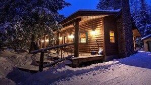 A log cabin with a stone chimney, wooden porch, and snow-covered surroundings. - Charming Adirondack Log Cabin PRIVATE BEACH ACCESS to Mirror Lake (Lake Placid)