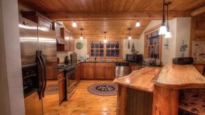 A kitchen with wooden cabinets, a stainless steel refrigerator, and a wooden island counter. - Charming Adirondack Log Cabin PRIVATE BEACH ACCESS to Mirror Lake (Lake Placid)