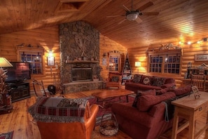 A cozy log cabin interior with a stone fireplace, wooden furniture, and a television.