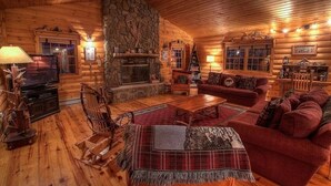 A cozy log cabin interior with a stone fireplace, wooden furniture, and a television. - Charming Adirondack Log Cabin PRIVATE BEACH ACCESS to Mirror Lake (Lake Placid)