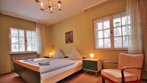 Ein Schlafzimmer mit einem Bett, Nachttischlampen, einem Sessel und einem Fenster mit Vorhängen.