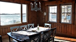 A wooden cabin with a dining area featuring a table set for four, large windows overlooking a body of water, and a chandelier hanging from the ceiling. - Ocean Front at Fortunes Rocks (Fortunes Rocks)