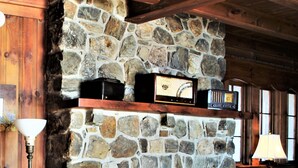A stone fireplace with a wooden mantel, a framed picture above it, and a small shelf with decorative items. - Ocean Front at Fortunes Rocks (Fortunes Rocks)